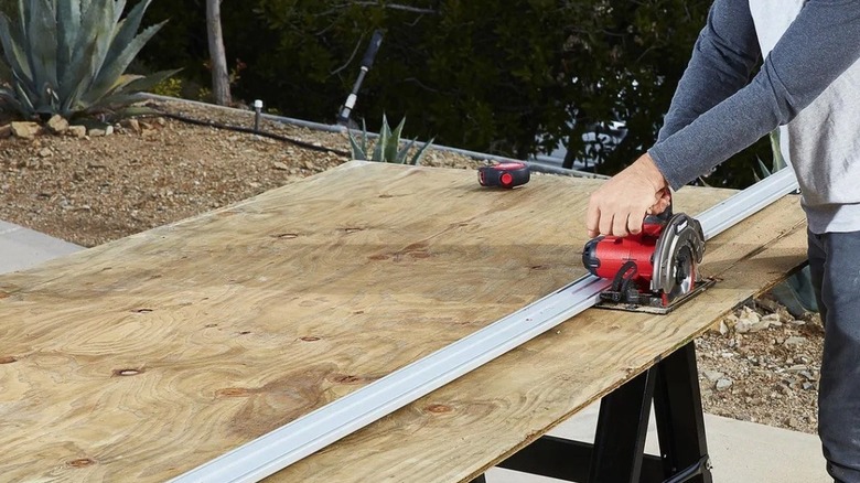 A person using a Quinn clamp guide to cut wood on a sawhorse