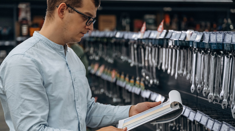 A person standing in front of a selection of wrenches on display, looking over stats on a clipboard