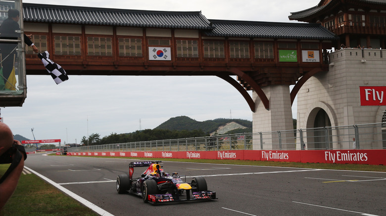 Car on a racing track passes under a wooden bridge with the South Korean flag.