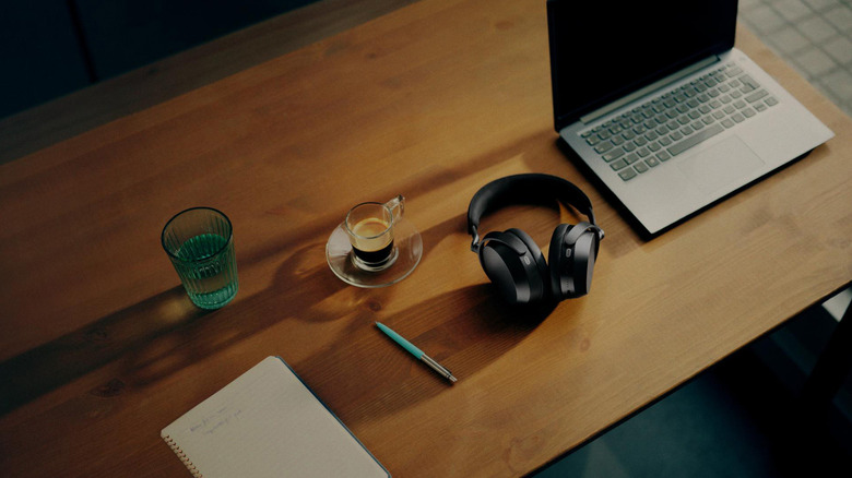 A pair of Sennheiser Momentum 5 headphones on a desk with other things.