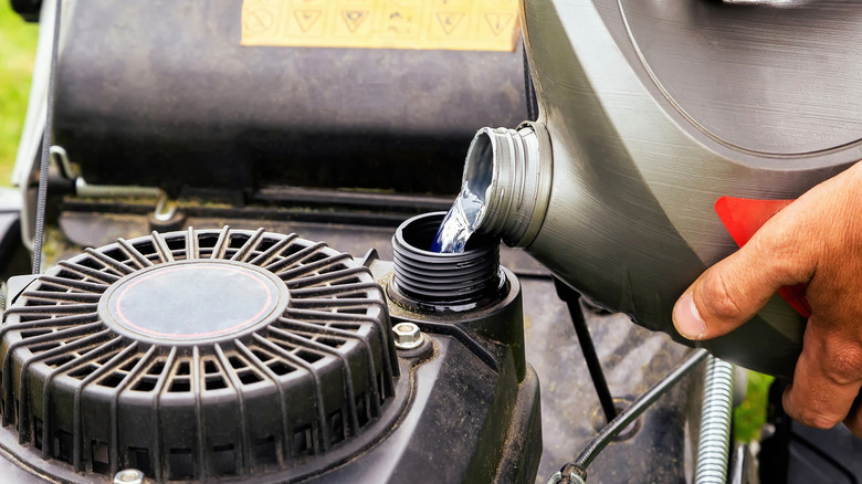 A person pouring fuel into a lawn mower.