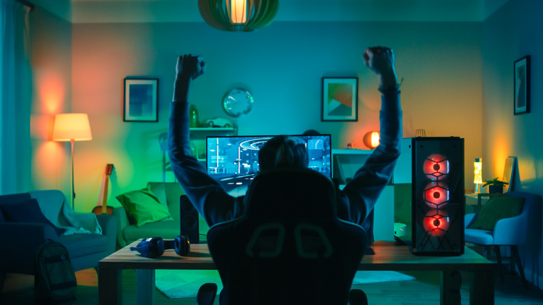 Young man sitting in his gaming chair raising his hands in a victory stance