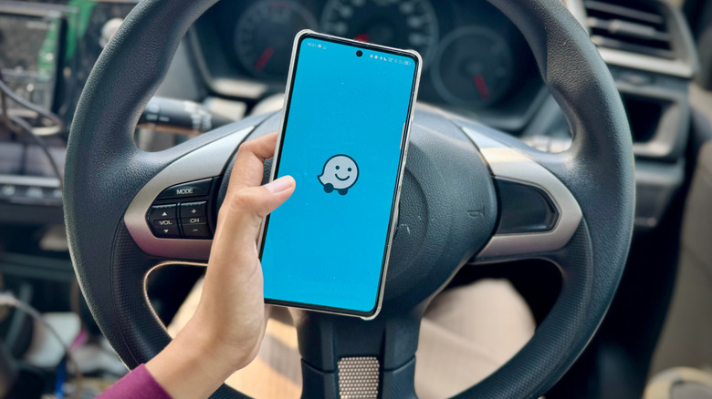 Person holding phone with Waze logo on the screen and steering wheel in background