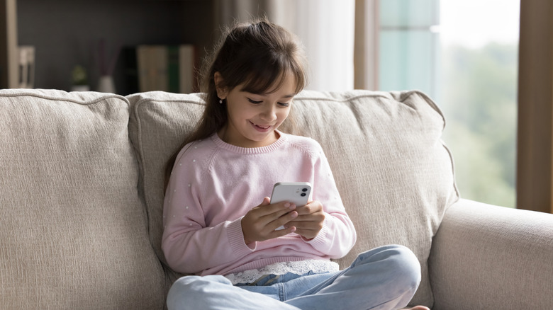 Smiling child using smartphone while sitting on couch