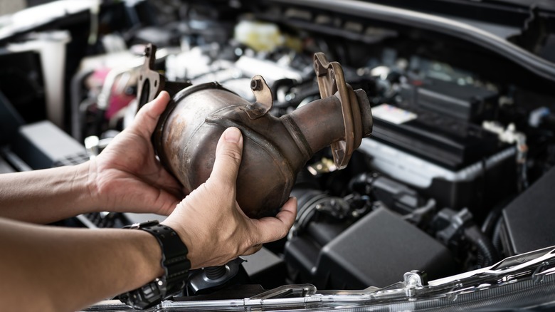 pair of hands holding catalytic converter 