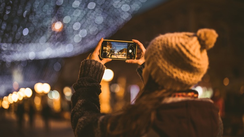 A person taking a photo of an evening street scene on their smartphone.