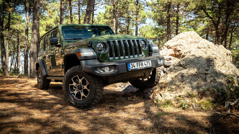 A green Jeep with a tire resting on a boulder.