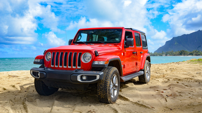 A red Jeep Wrangler on the beach.