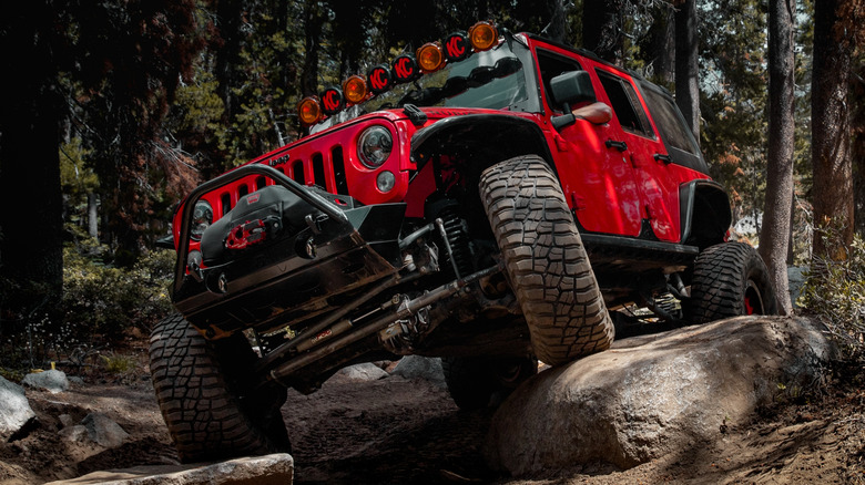 A red Jeep driving over some boulders.