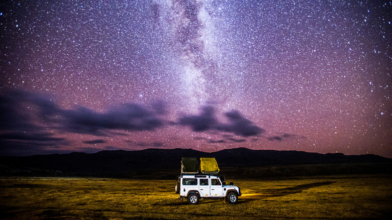 A white Jeep with a tent mounted on top of it in a field under a sky full of stars.