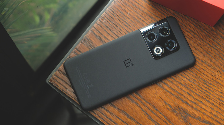 A OnePlus 10 smartphone resting on a wooden table with a red box on top.