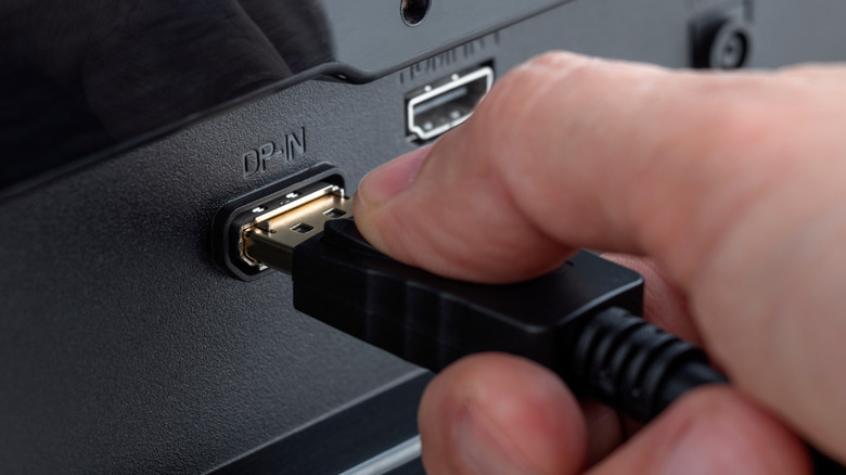 A man connecting a DisplayPort cable into its appropriate port in a monitor