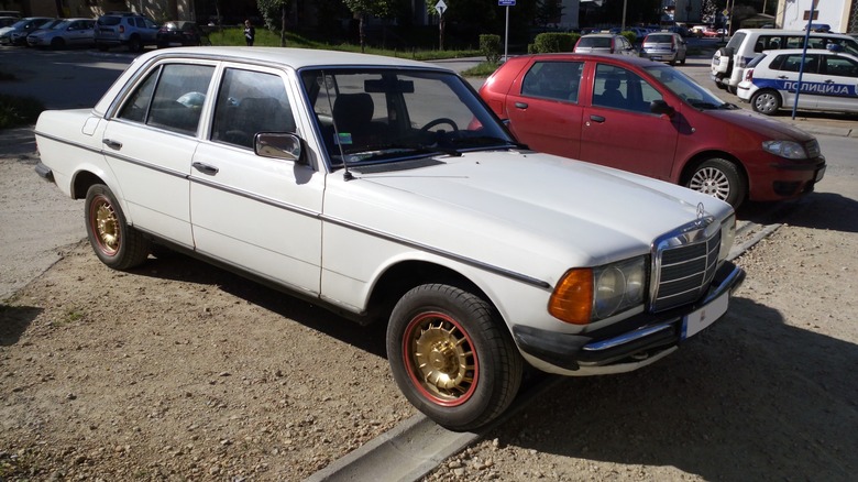Mercedez-Benz W123 parked on dirt next to red car