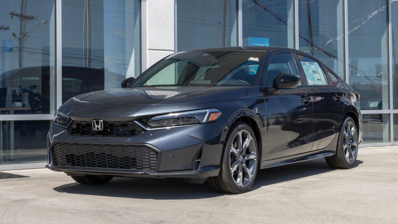 A brand new gray Honda Civic Touring hybrid parked in front of a dealership.