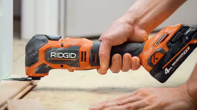 A person using a Ridgid multitool on the ground.