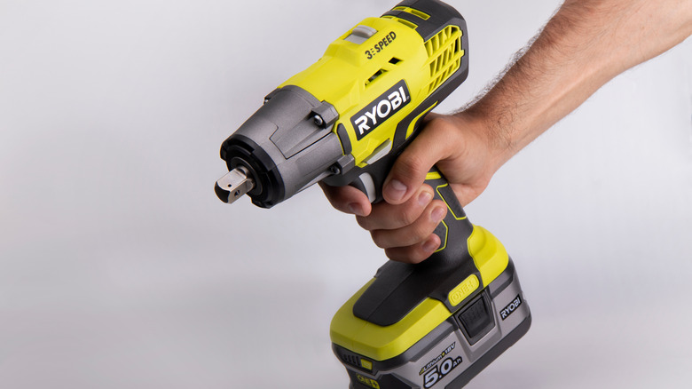 A person holding a green and black Ryobi impact gun.