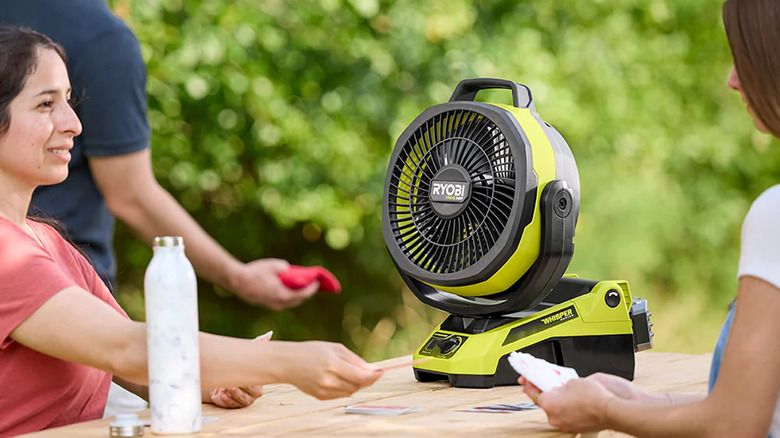 Three people using a 18V One+ HP Brushless Hybrid 9 Oscillating Fan on a picnic bench.