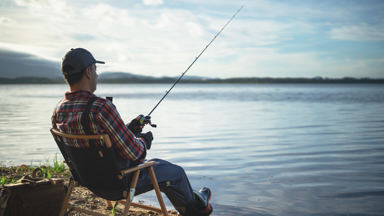 A man sitting on a chair, fishing by a lake