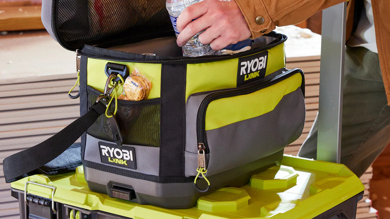 A hand placing a bottle of water in the Ryobi soft-sided cooler