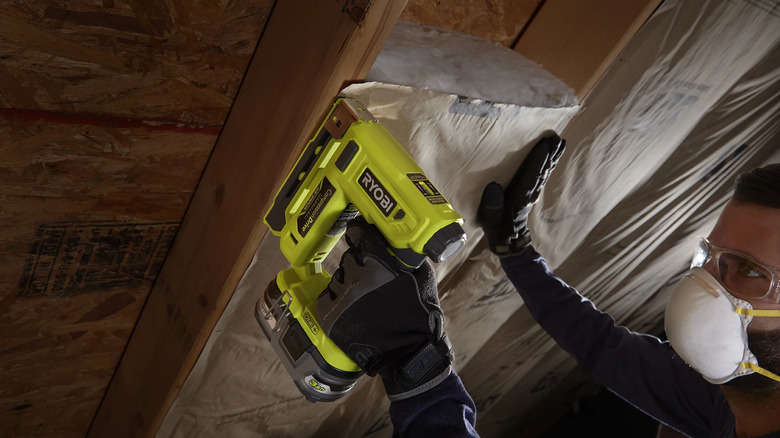 DIYer using a Ryobi P317 stapler to secure insulation between attic rafters