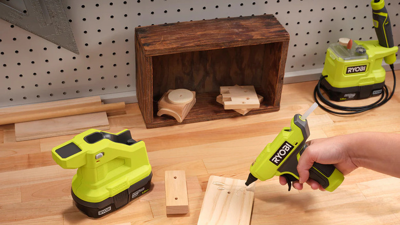 A Ryobi Glue Gun being used on a piece of wood on a desk.