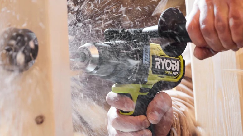 A Ryobi hammer drill drilling through wood.