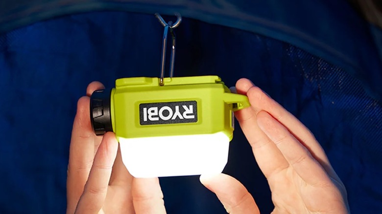 A person hanging the Ryobi USB Lithium Cordless Compact Area Light in a tent.