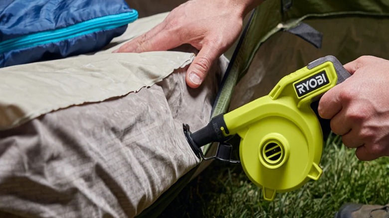 A person inflating an air mattress with the Ryobi USB Lithium Cordless High Volume Inflator.