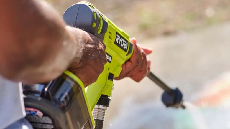 Close-up of two hands using ONE+ 18V EZClean 320 PSI 0.8 GPM Cold Water Power Cleaner on driveway