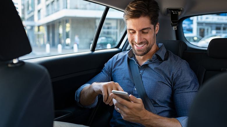 man in back seat of car texting