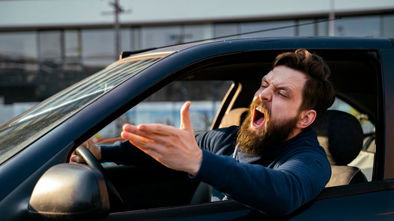 man in car shouting out the window, waving an arm