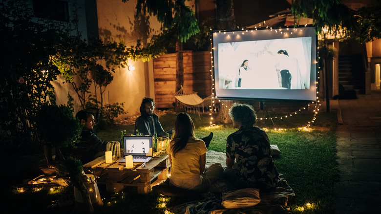 People watching a film outdoors with a projector screen.