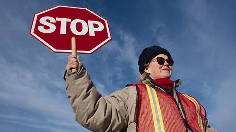 A crossing guard holds stop sign in a hi-vis vest.