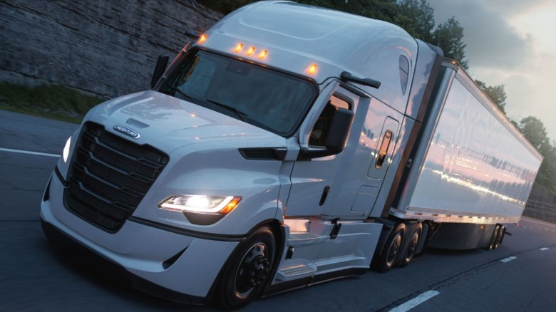A white Freightliner Cascadia driving on a highway at dusk
