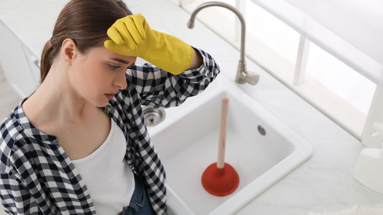 Woman showing fatigue after using plunger in her kitchen sink