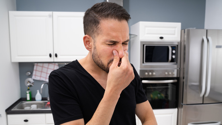 Person holding their nose due to a bad smell in the kitchen