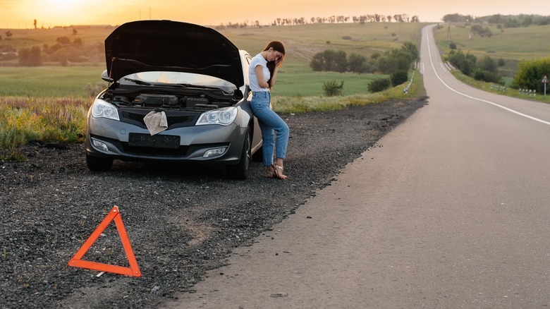 A distressed car owner on the side of their road with a broken down vehicle, its hood up