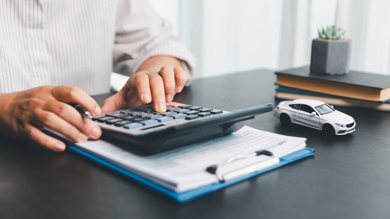 A person seated at a desk with a toy car, using a calculator to calculate vehicle ownership costs