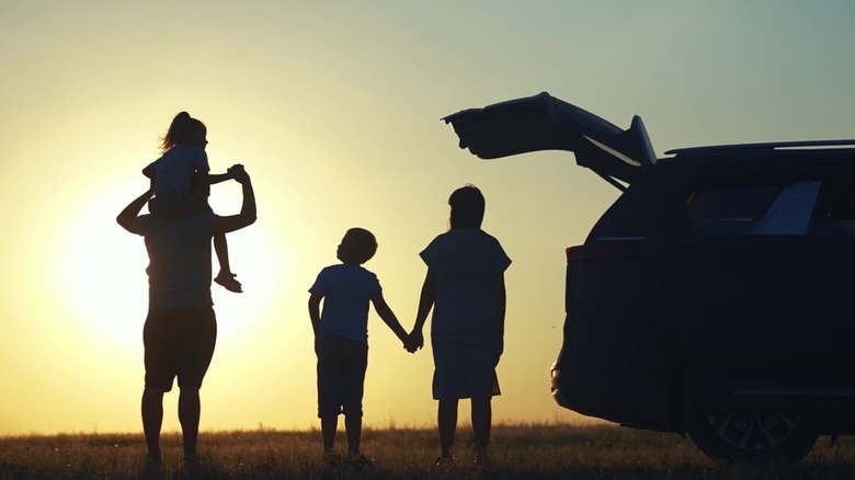 A family enjoying a sunset, standing towards the rear of their van