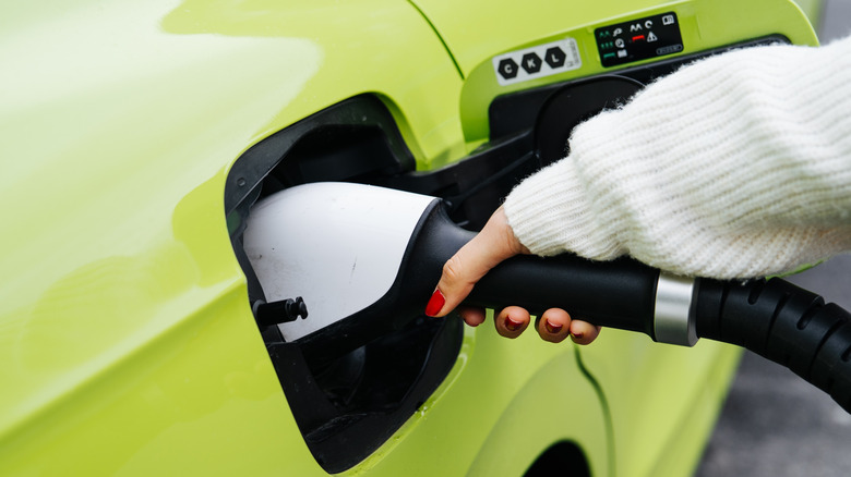 Close-up of a women's hand plugging in a lime green electric vehicle to a charger