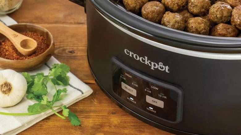 A Crockpot housing meatballs next to herbs and spices.