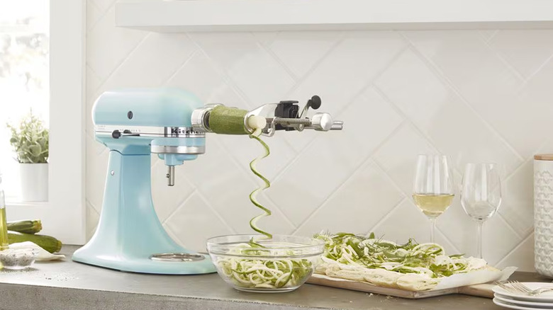 A light blue KitchenAid stand mixer with a spiralizer attachment making zucchini noodles.