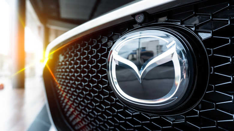 A close-up of a Mazda badge on the front of a Mazda car with sun in the background.