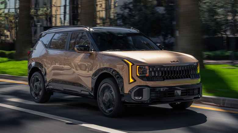 A bronze/gold Kia Seltos SUV being driven down a city road.