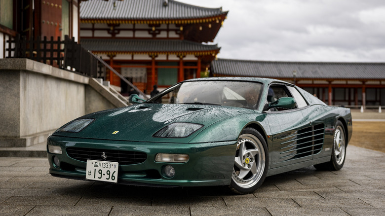 A green Ferrari 512M parked in front of a temple.