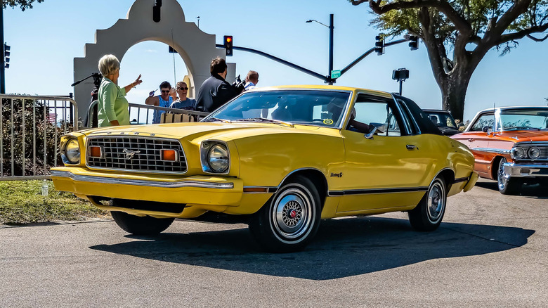 A yellow Ford Mustang II driven on the road.