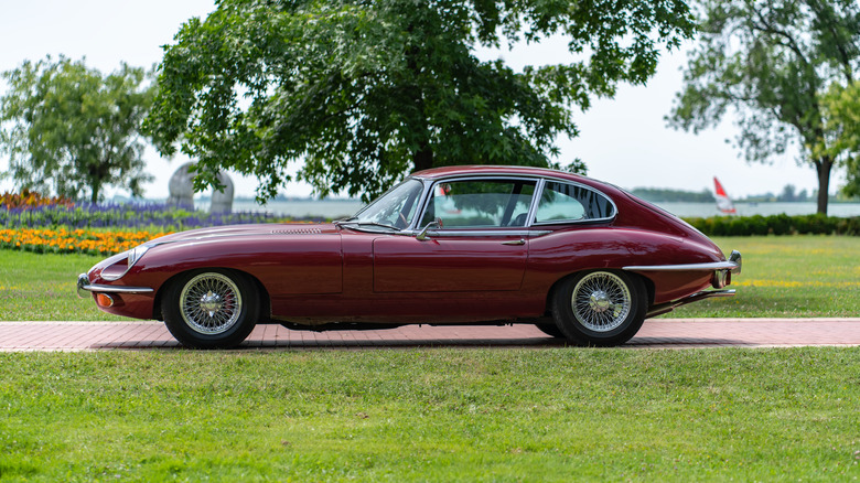 A side-profile view of a vintage red Jaguar parked on a lawn.