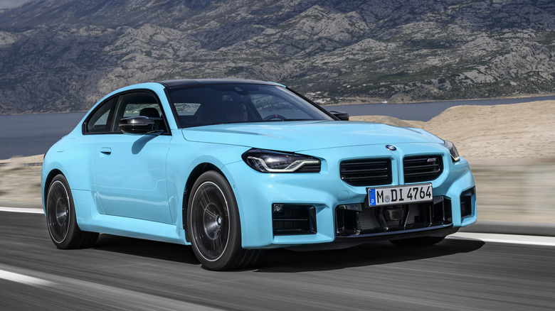 Front 3/4 view of blue BMW M2 driving on mountain road.