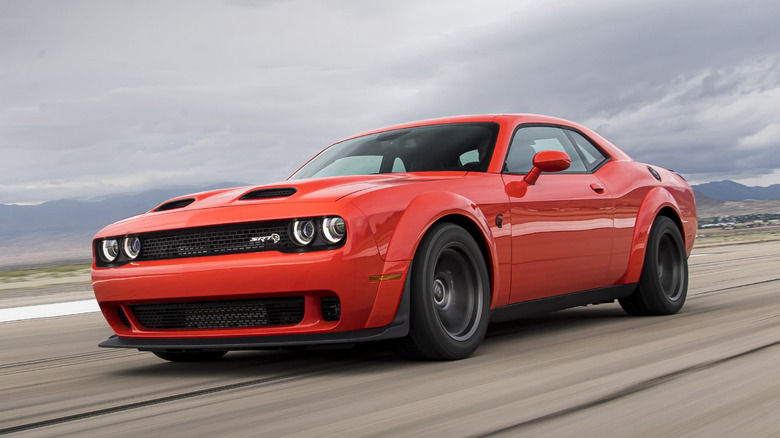 Front 3/4 view of orange Dodge Challenger widebody driving on airport runway.
