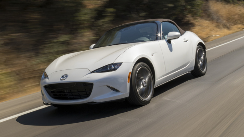 Front 3/4 view of white Mazda MX-5 Miata driving on highway.